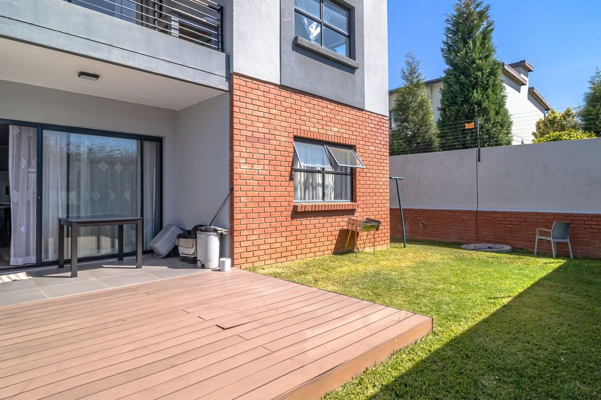Rear view of the apartment featuring a timber deck, small private lawn, brick facade, and secure boundary wall with electric fencing.