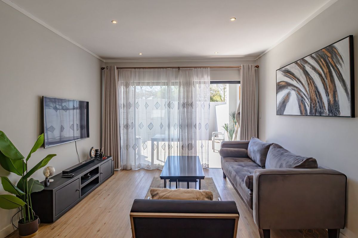 A well-maintained living room featuring laminate flooring, recessed downlighting, and a large sliding glass door providing access to an outdoor patio area.
