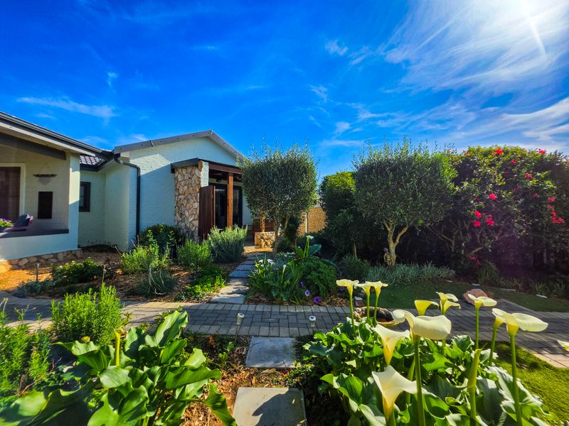 A beautifully landscaped rear garden featuring a stone-clad exterior wall, a timber pergola, and a paved walkway leading to the home.