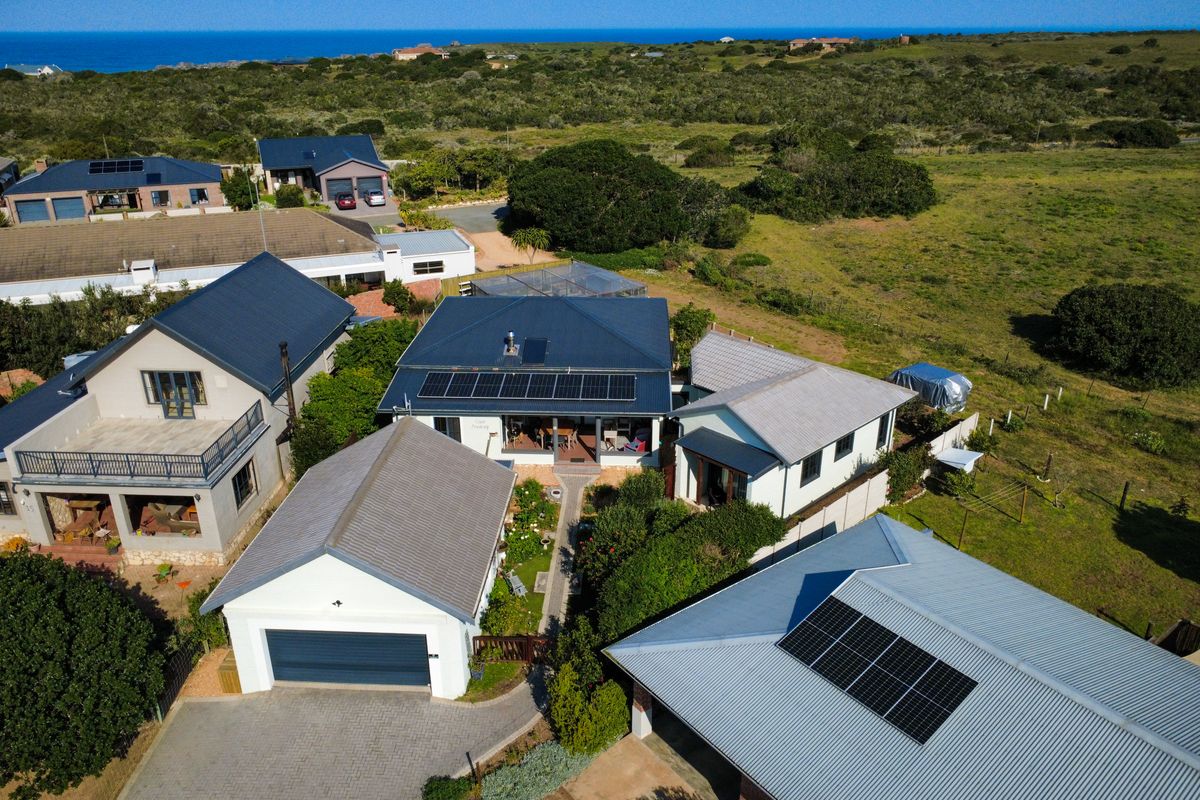 Aerial view of a residential property featuring multiple buildings with metal roofs, solar panel installations, paved driveways, and surrounding landscaped garden areas.