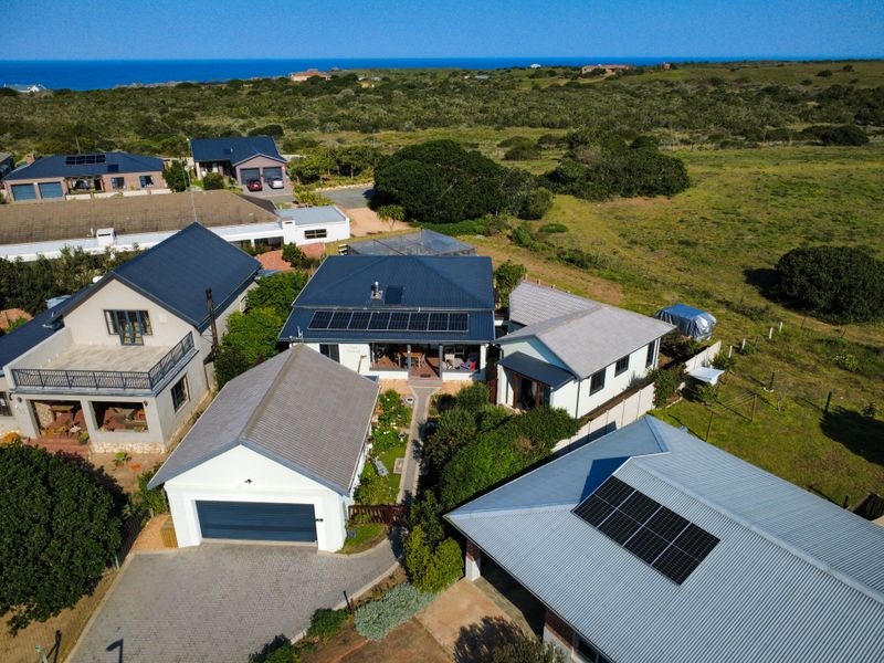 Aerial view of a residential property featuring multiple buildings with metal roofs, solar panel installations, paved driveways, and surrounding landscaped garden areas.
