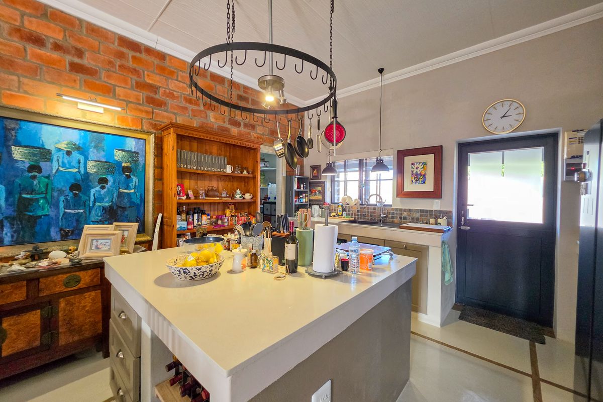 A characterful kitchen featuring an exposed brick wall, a central island with a hanging pot rack, and direct access to the exterior.