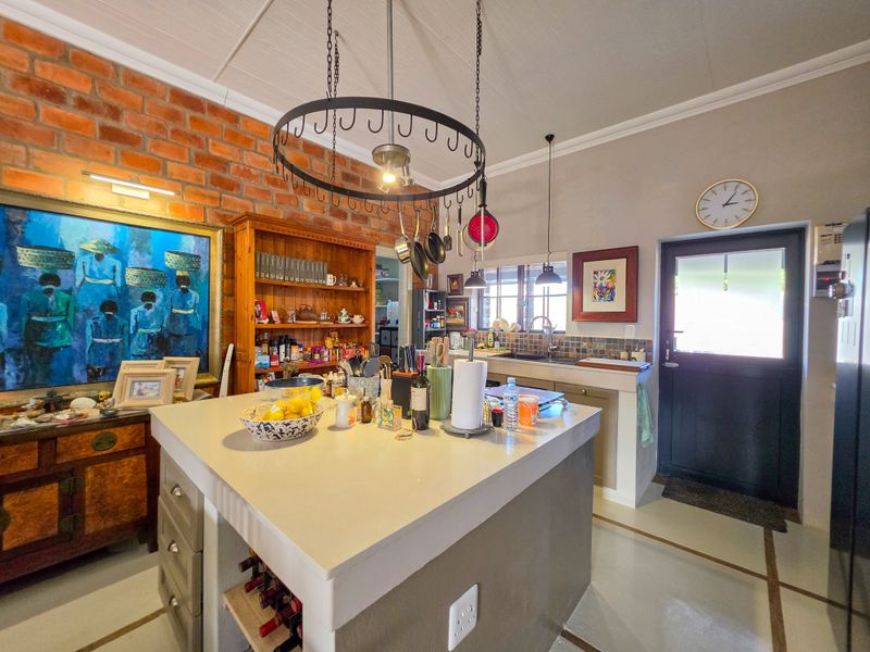 A characterful kitchen featuring an exposed brick wall, a central island with a hanging pot rack, and direct access to the exterior.