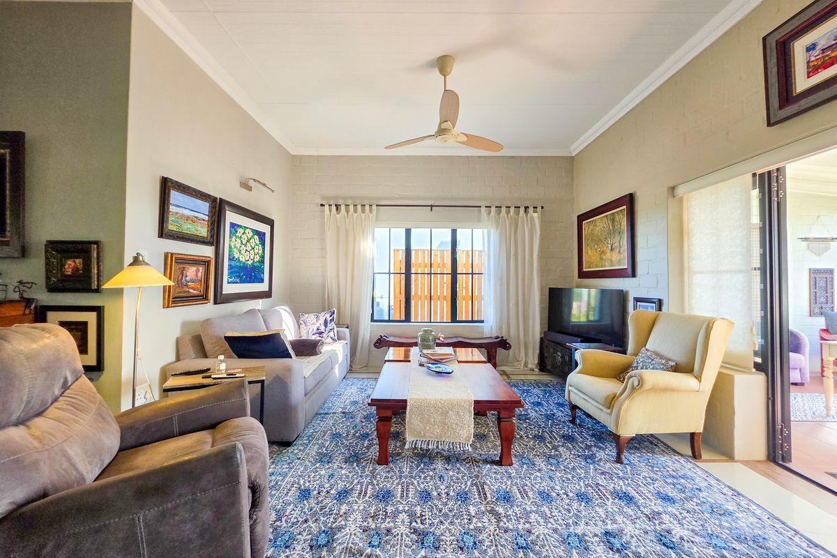 A comfortable living room featuring a ceiling fan, coved cornicing, and large sliding glass doors that provide access to the outdoor area.