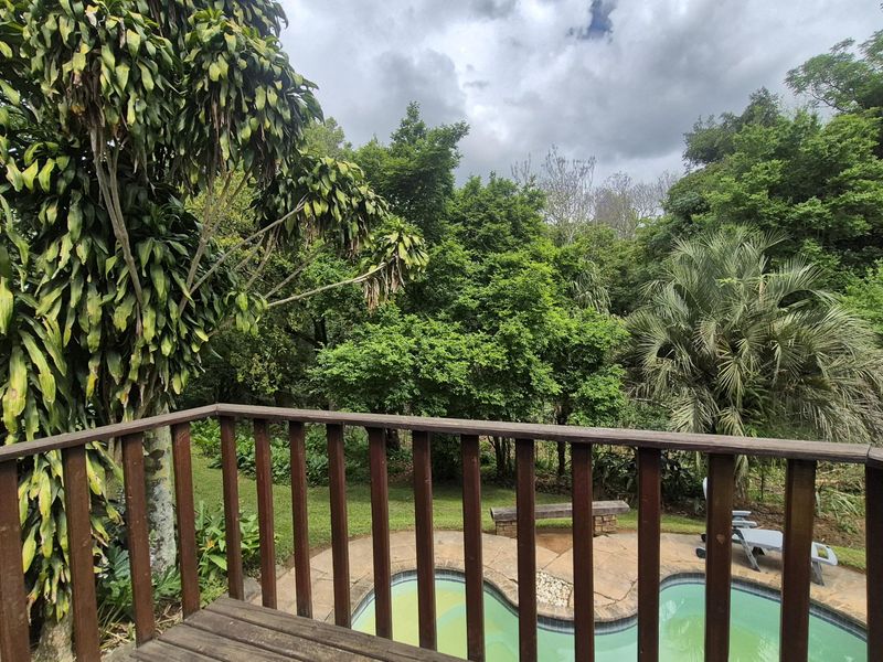 Elevated wooden balcony overlooking a swimming pool and lush garden area, providing a peaceful outdoor space.