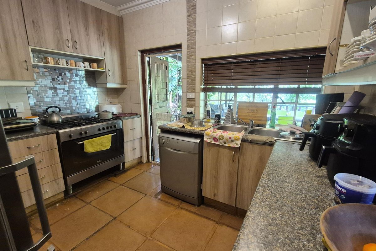 Functional kitchen featuring wood-look cabinetry, gas stove with oven, tiled backsplash, and double sink with direct access to the outdoor area.