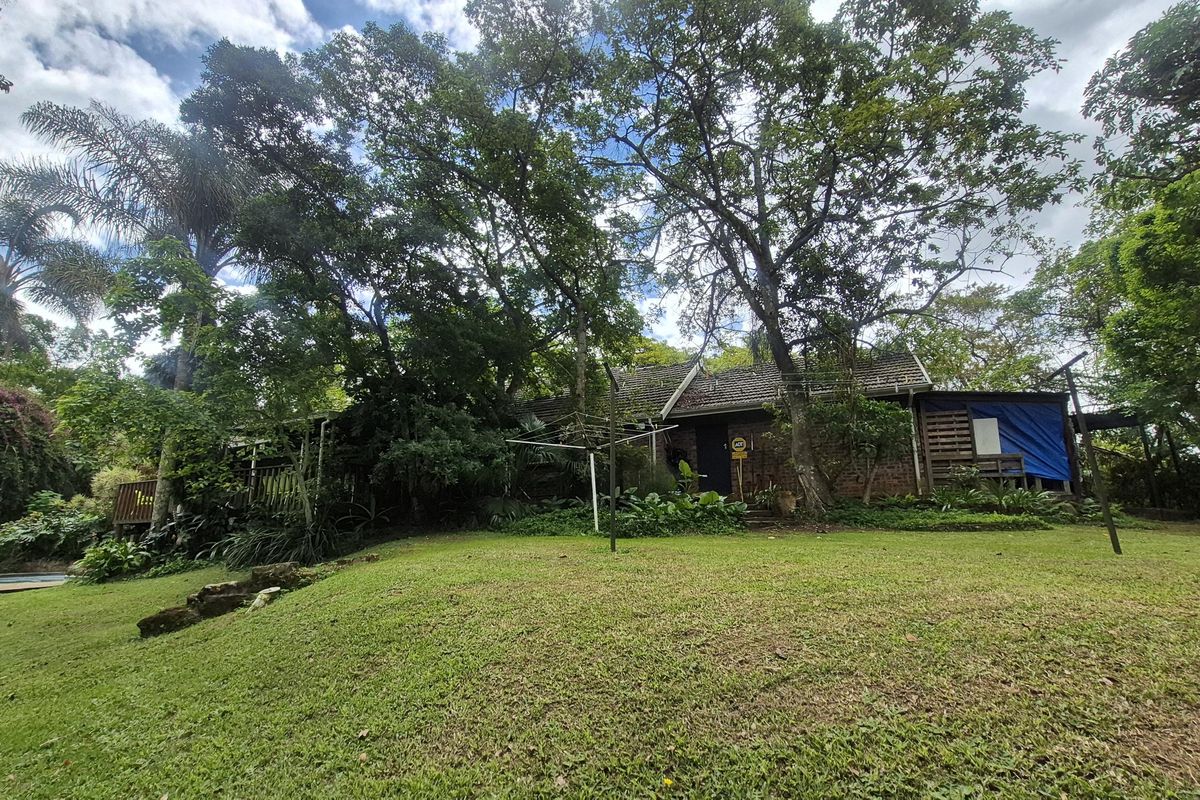 A view of the rear exterior of the house, featuring a brick facade, tiled roof, and a spacious, tree-lined garden area.
