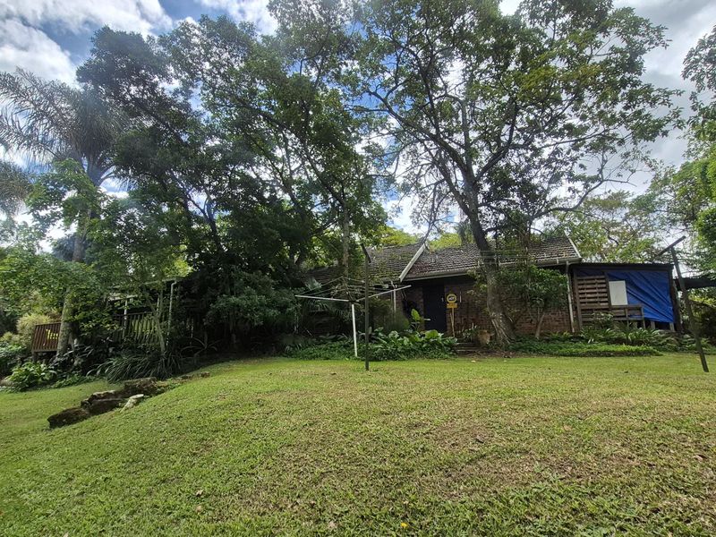 A view of the rear exterior of the house, featuring a brick facade, tiled roof, and a spacious, tree-lined garden area.