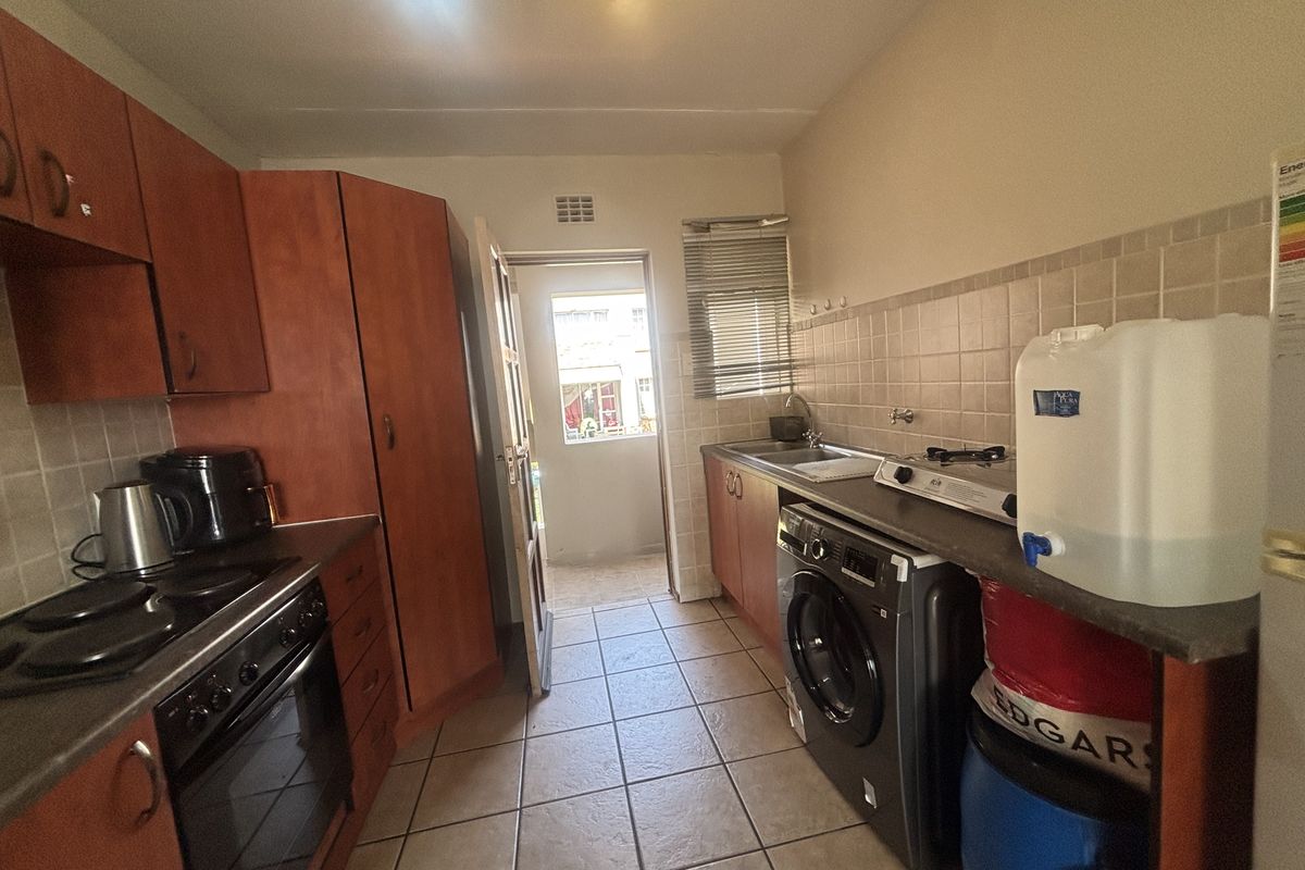 Functional kitchen featuring wood-look cabinetry, tiled backsplash, built-in oven and hob, and dedicated plumbing for a washing machine with direct access to the exterior.