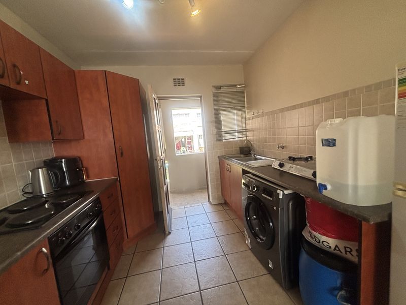 Functional kitchen featuring wood-look cabinetry, tiled backsplash, built-in oven and hob, and dedicated plumbing for a washing machine with direct access to the exterior.