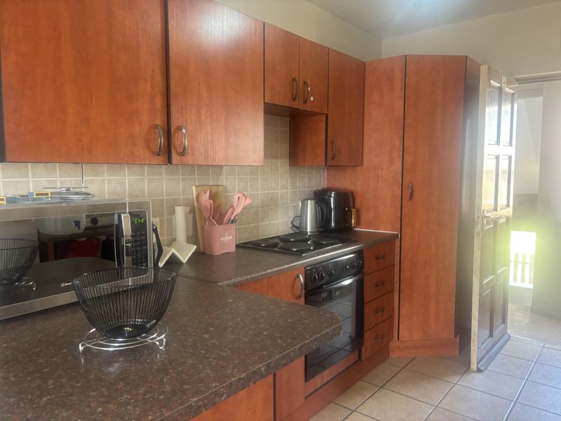 A functional kitchen featuring wood-look laminate cabinetry, dark countertops, built-in oven, electric hob, and tiled flooring with direct access to an exterior area.