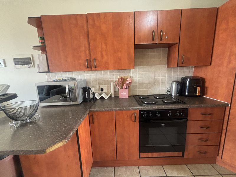 A functional kitchen featuring wood-look laminate cabinetry, dark countertops, a tiled backsplash, and a built-in electric oven with a hob.