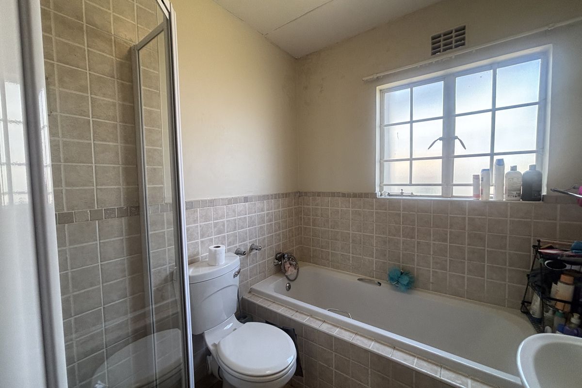 A functional bathroom featuring a shower enclosure, bathtub, and toilet with neutral wall tiling and a window for natural light.