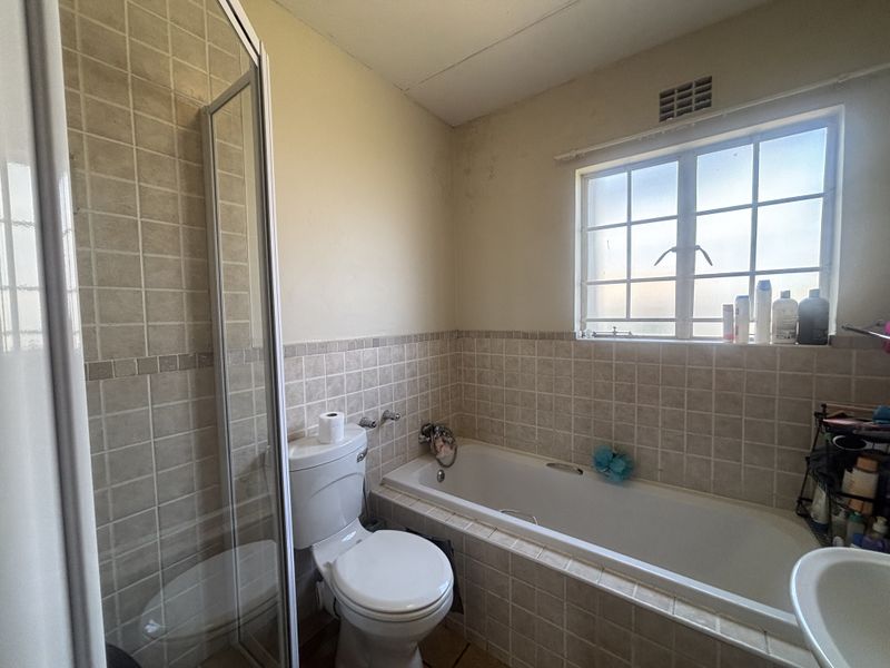 A functional bathroom featuring a shower enclosure, bathtub, and toilet with neutral wall tiling and a window for natural light.