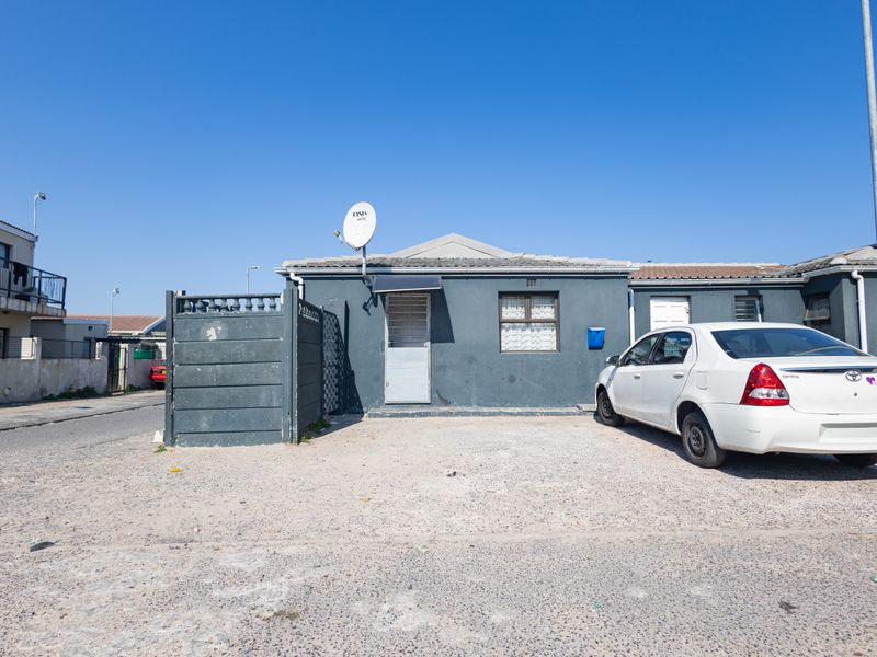 Front exterior view of a single-story house featuring a gravel driveway, security gate, and satellite dish installation.