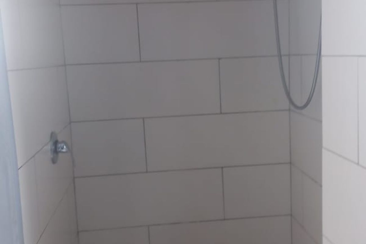 A compact bathroom shower enclosure featuring tiled walls, a shower mixer, and a pedestal basin with a chrome mixer tap.