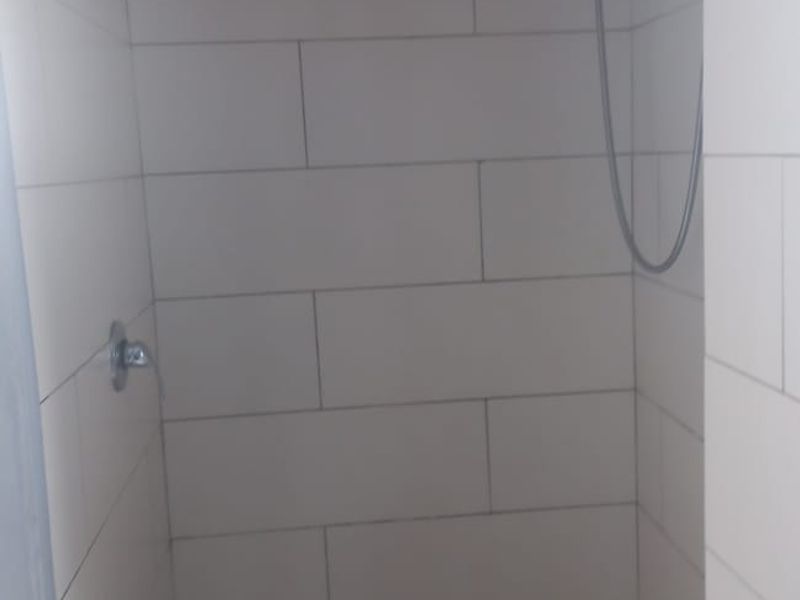 A compact bathroom shower enclosure featuring tiled walls, a shower mixer, and a pedestal basin with a chrome mixer tap.