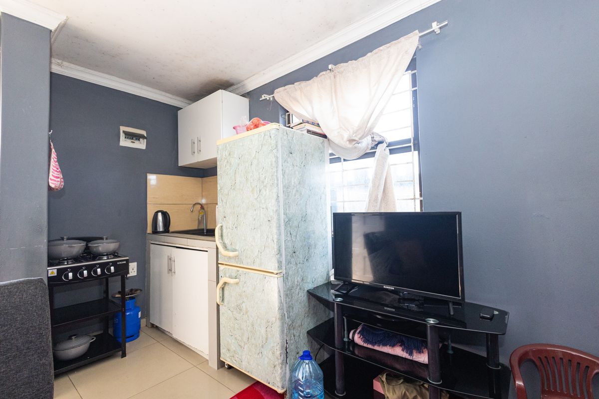 Compact kitchen area featuring basic cabinetry, a sink, tiled splashback, and security bars on the window, with visible signs of ceiling wear.