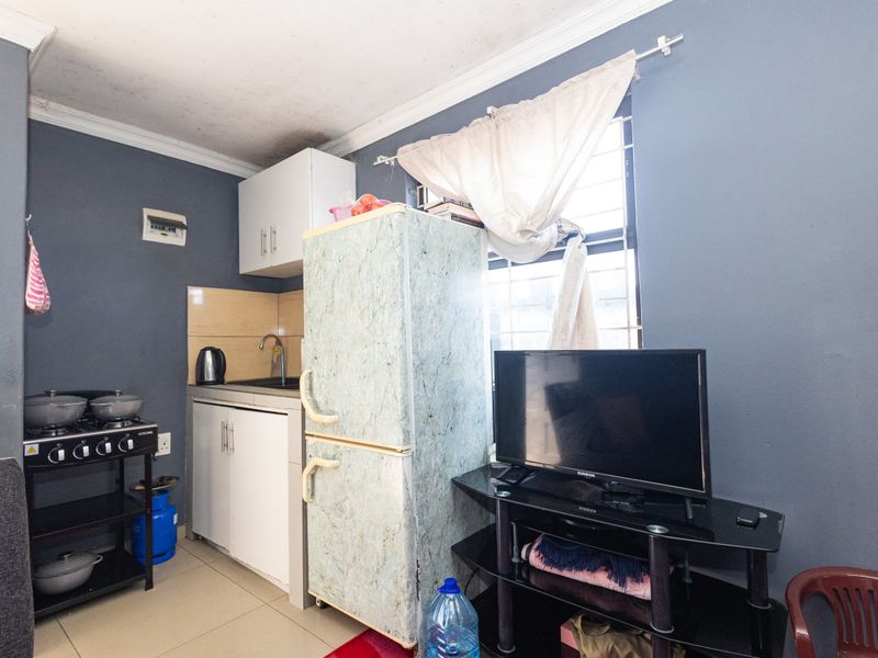 Compact kitchen area featuring basic cabinetry, a sink, tiled splashback, and security bars on the window, with visible signs of ceiling wear.