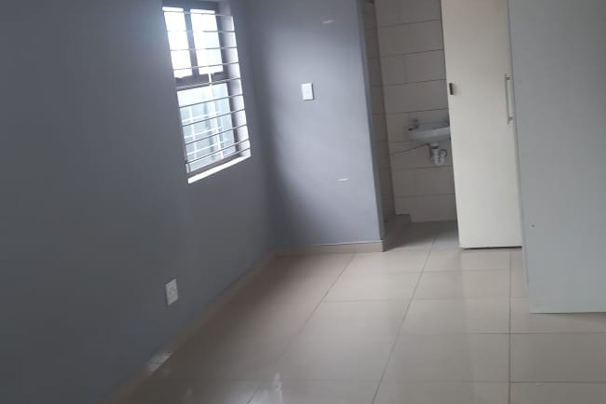 A clean, empty bedroom featuring tiled flooring, a built-in cupboard, and an en-suite bathroom entrance.