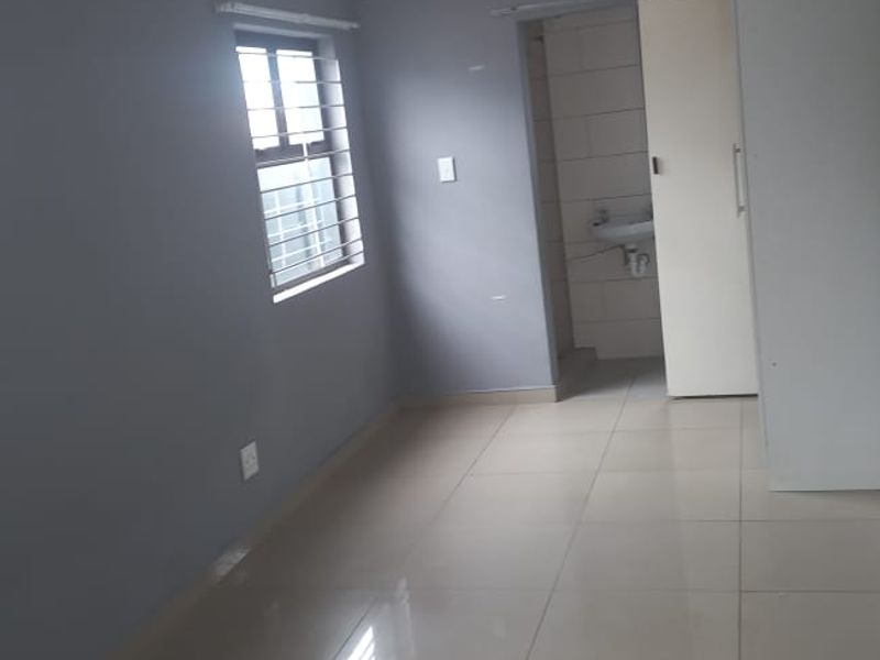 A clean, empty bedroom featuring tiled flooring, a built-in cupboard, and an en-suite bathroom entrance.