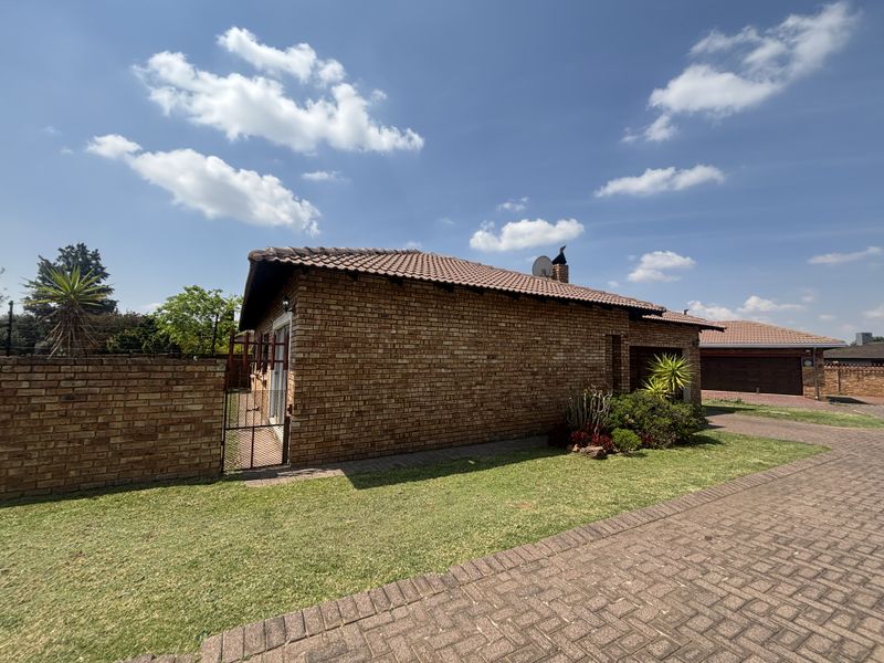 A view of the front exterior of a face brick house featuring a tiled roof, paved driveway, and a private gated entrance.