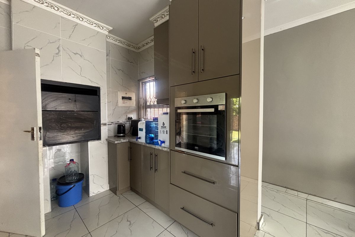 Modern kitchen featuring high-gloss cabinetry, built-in oven, marble-look tiling, and a built-in braai area with decorative ceiling cornices.