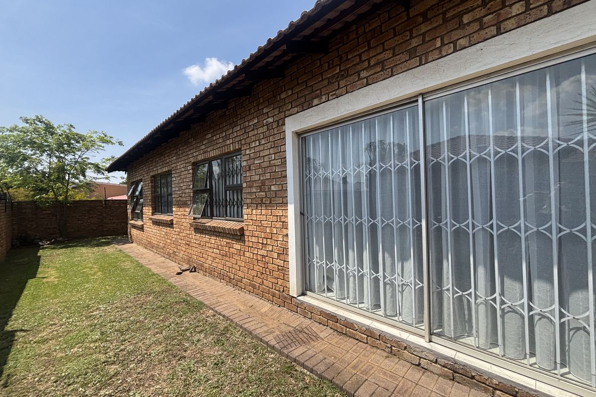 Rear view of the property featuring a face brick facade, tiled roof, sliding glass door with security gate, and a small lawn area.