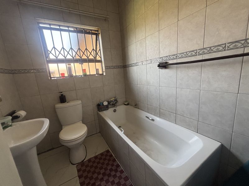 A functional bathroom featuring a pedestal basin, toilet, and bathtub with neutral wall tiling and a security gate on the window.