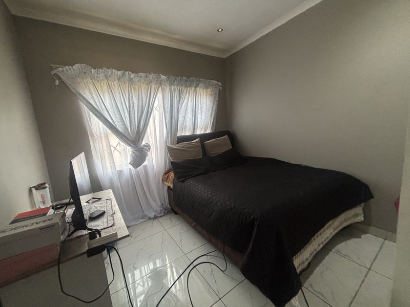 A functional bedroom featuring polished tiled flooring, neutral wall tones, and recessed ceiling lighting with security bars on the window.