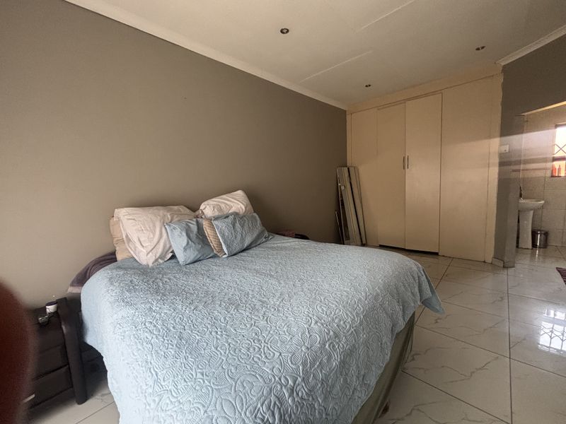 Spacious bedroom featuring tiled flooring, built-in cupboards, and recessed downlights, with an adjoining en-suite bathroom visible.