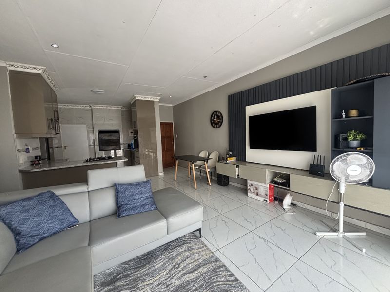 Spacious open-plan living area featuring modern marble-look floor tiles, a sleek built-in media wall, and a contemporary kitchen with integrated appliances.
