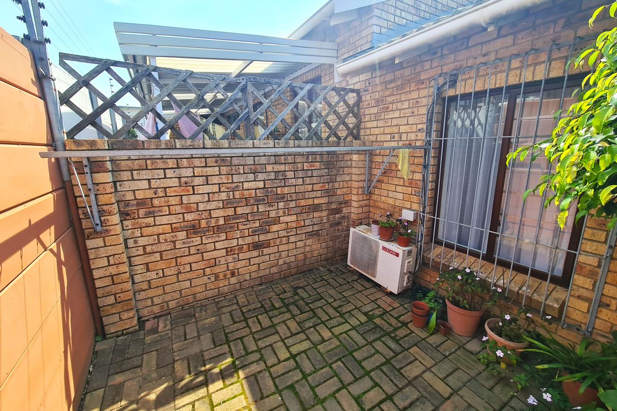A private rear courtyard area featuring brick walls, paved flooring, security bars on windows, and an external air conditioning unit.