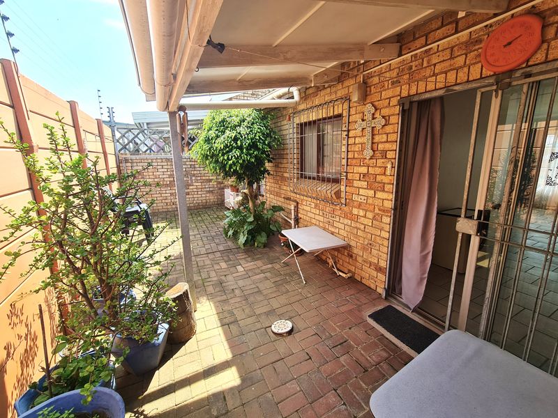 A covered brick-paved patio area featuring facebrick walls, security gates, and sliding door access to the interior living space.