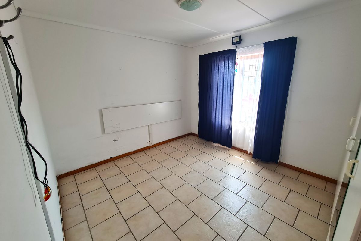 An empty bedroom featuring tiled flooring, a window with security bars, and basic lighting. The room requires cosmetic updates to the walls and fixtures.