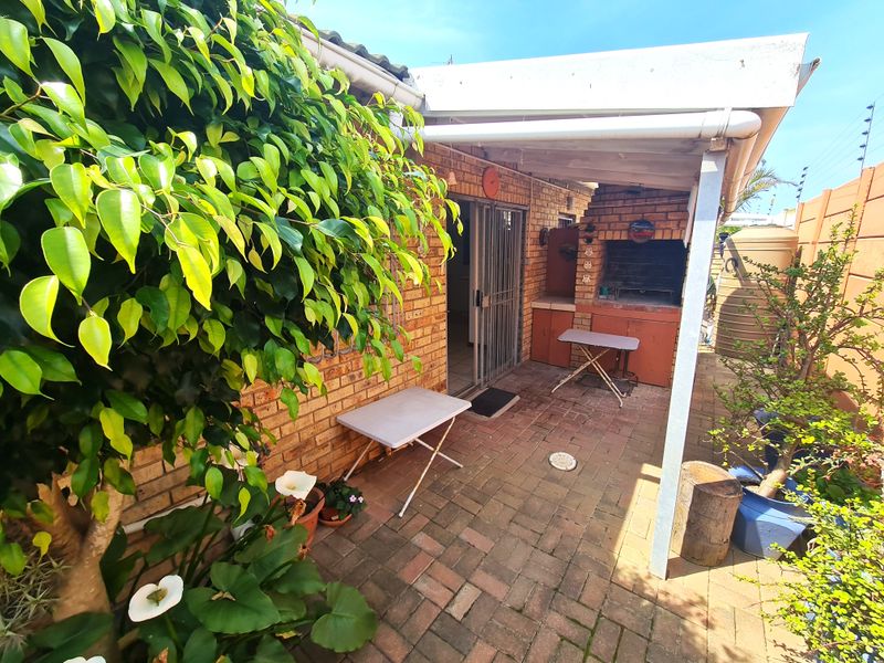 Covered outdoor patio area featuring a built-in brick braai, paved flooring, and direct access to the interior via a sliding door.