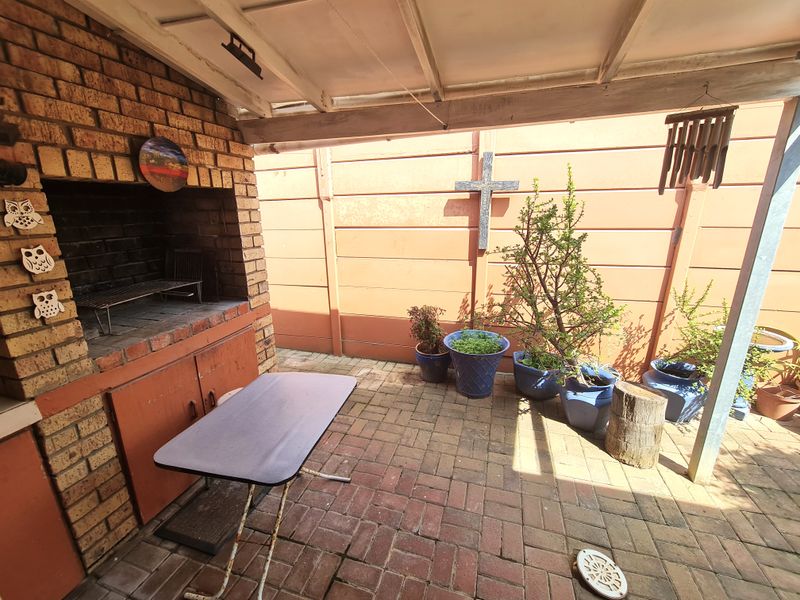 Covered outdoor patio area featuring a built-in brick braai and paved flooring, enclosed by a precast concrete boundary wall.