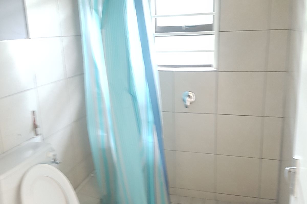 A compact bathroom featuring tiled walls and flooring, a walk-in shower area, and a standard toilet.
