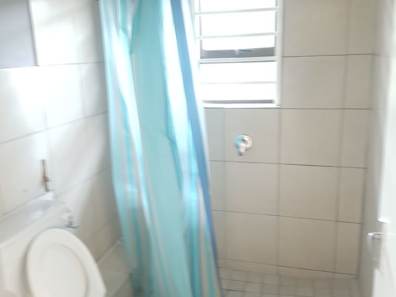 A compact bathroom featuring tiled walls and flooring, a walk-in shower area, and a standard toilet.