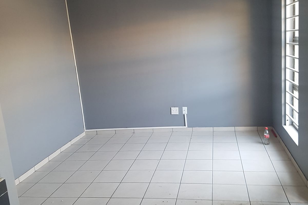 An empty bedroom featuring grey painted walls, tiled flooring, and a window fitted with security bars.