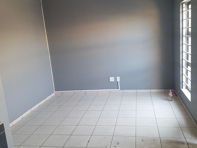 An empty bedroom featuring grey painted walls, tiled flooring, and a window fitted with security bars.
