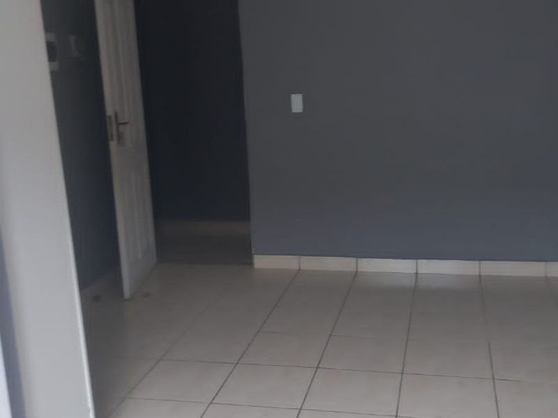 An empty bedroom featuring neutral grey walls, tiled flooring, and a built-in cupboard, providing a blank canvas for personalization.
