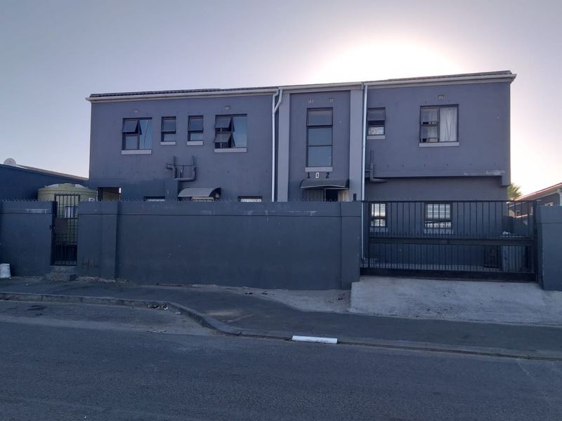 Front elevation of a multi-story residential building featuring a secure perimeter wall, gated driveway access, and exterior security fencing.