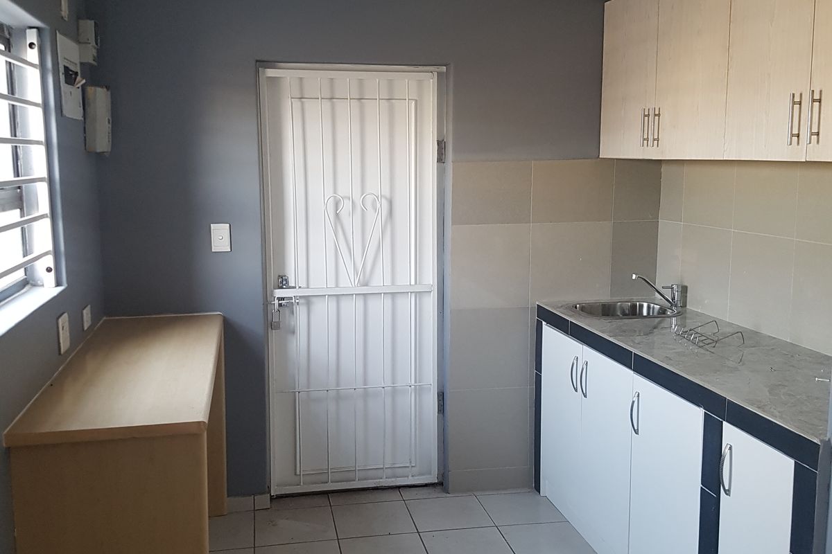 A functional kitchen featuring built-in cabinetry, laminate countertops, a stainless steel sink, and tiled flooring with direct access to an exterior security door.