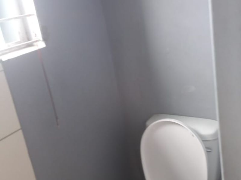 A compact bathroom featuring a standard toilet, tiled wall sections, and a window with security bars.