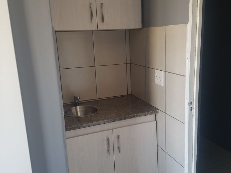 A compact scullery or utility area featuring built-in cabinetry, a stainless steel sink, and tiled splashbacks.