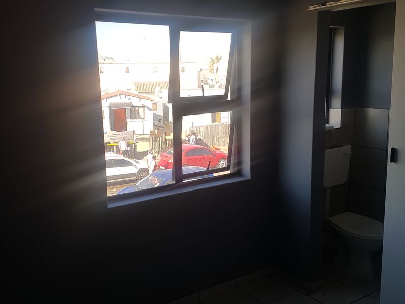 An empty bedroom featuring tiled flooring, an aluminium window, and an attached en-suite toilet facility.