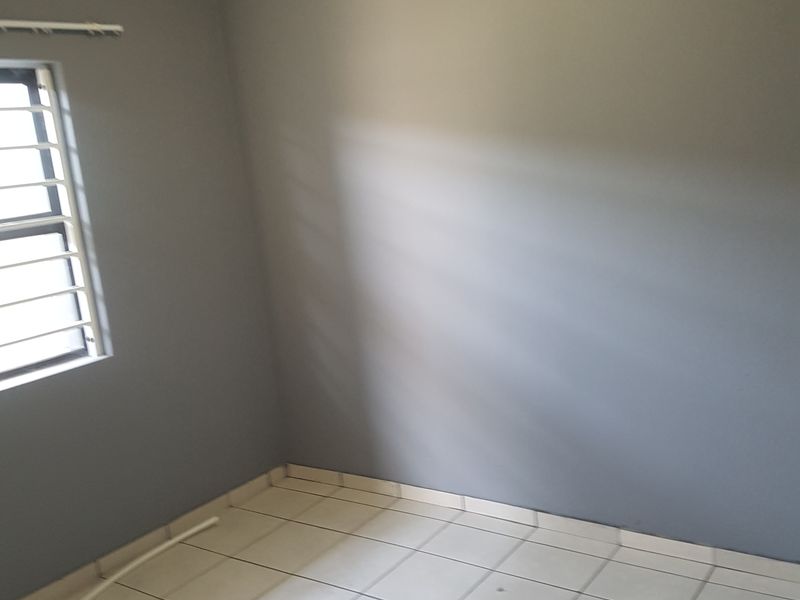 An empty bedroom featuring neutral grey walls, tiled flooring, and a window fitted with security bars.