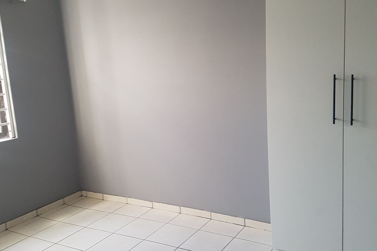A clean, empty bedroom featuring neutral grey walls, white tiled flooring, and modern built-in cupboards.