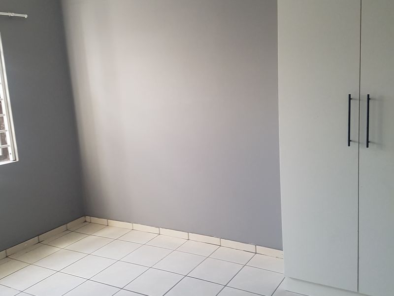 A clean, empty bedroom featuring neutral grey walls, white tiled flooring, and modern built-in cupboards.